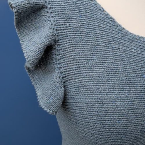 Close up of a hand knitted ruffle on the shoulder of a blue cotton and silk top