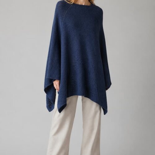 Woman modeling dark navy handmade knitted poncho by INESKA on gray background.