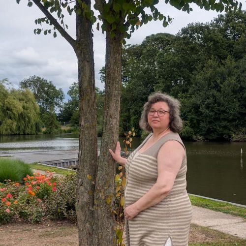 Woman wearing handmade linen knit long vest by INESKA in a garden by the water, natural fibres, handgebreid vest, slow fashion Netherlands