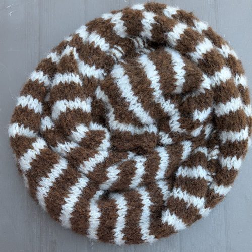 Warm brown alpaca scarf with cream stripes by INESKA — coiled on a garden table