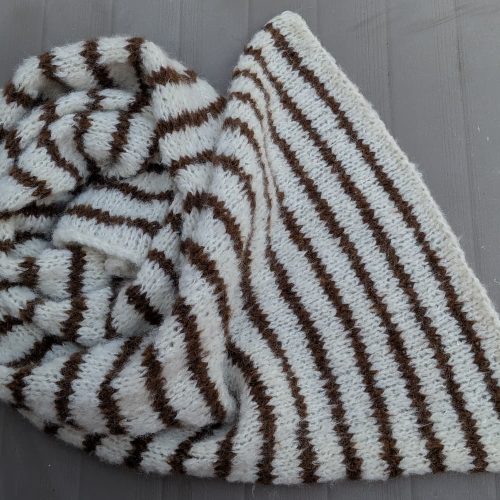 Handknitted cream alpaca scarf with brown stripes by INESKA — folded on a garden table