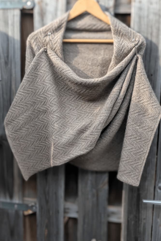 Hand-knitted mohair merino cashmere scarf in taupe with herringbone texture and two decorative pins, draped on a wooden hanger