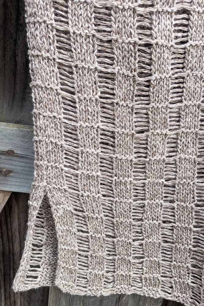 Detail of the hem and openwork stitch pattern of the hemp knit tunic against weathered wood