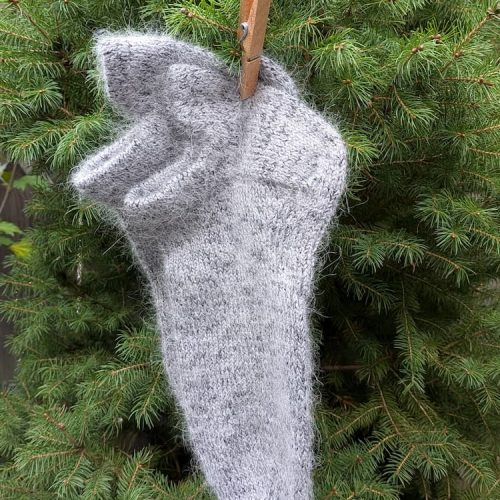 Grey fluffy hand knitted merino and mohair sleeping sock hanging on a wooden clothespin among fir branches